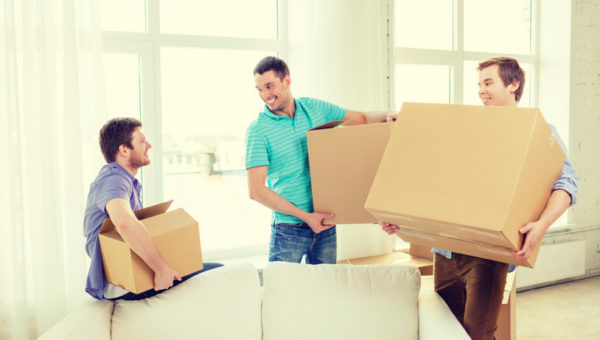 smiling male friends carrying boxes at new place