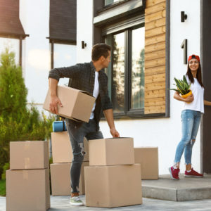 Happy couple with moving boxes and household stuff near their new house on sunny day