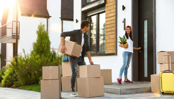 Happy couple with moving boxes and household stuff near their new house on sunny day