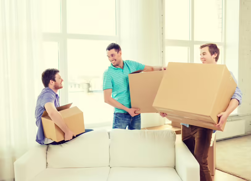smiling male friends carrying boxes at new place